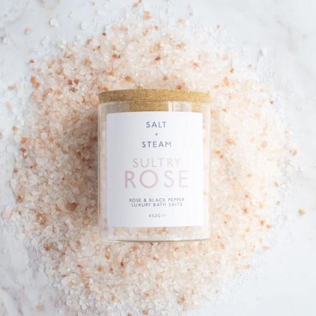 glass jar of bath salts laying on a pile of pink salt gems
