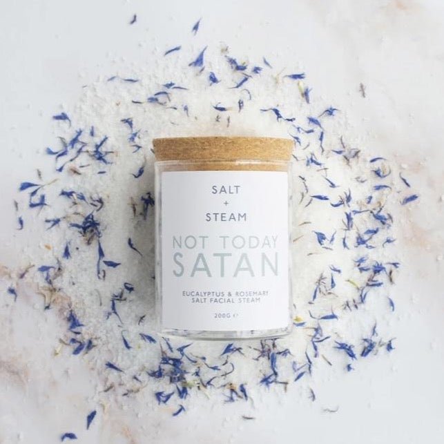 a corked glass jar laid on a pile of salt and purple petals