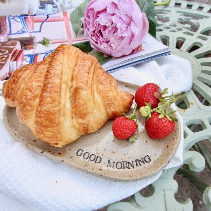 Ceramic oval plate holding a croissant and strawberries, next to an open magazine