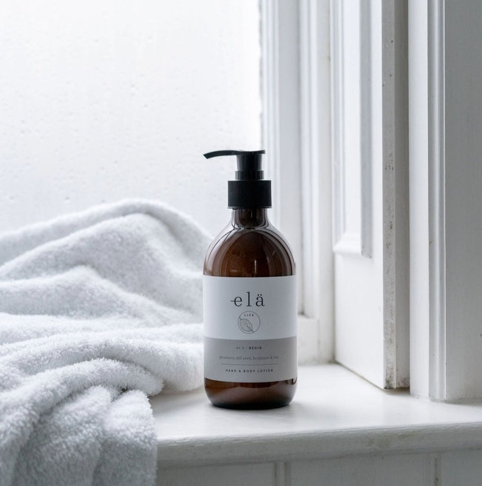 amber glass bottle with a pump dispenser, pictured on a window ledge beside a fluffy towel