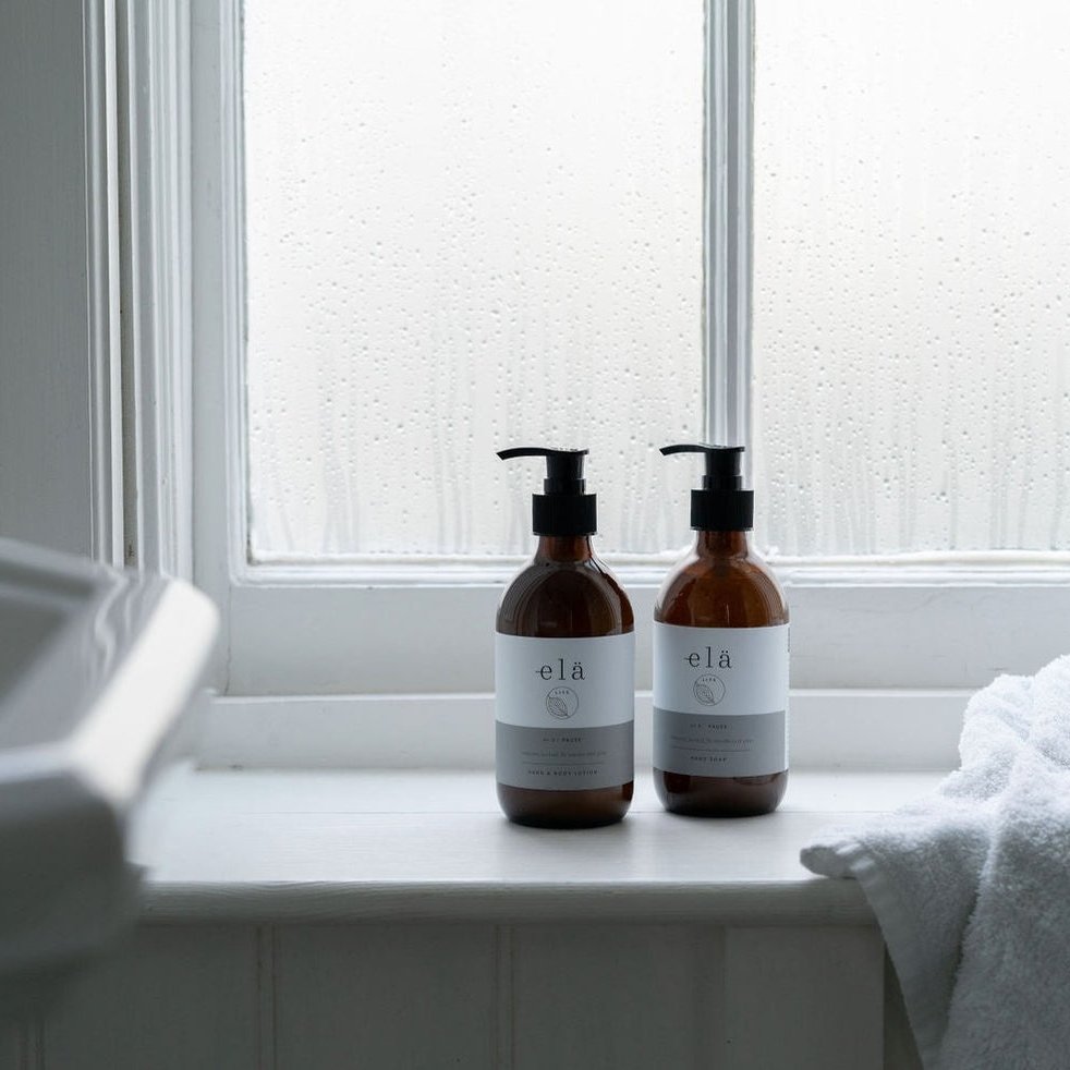 2 amber glass bottles with pump dispensers stood in front of a rainy window
