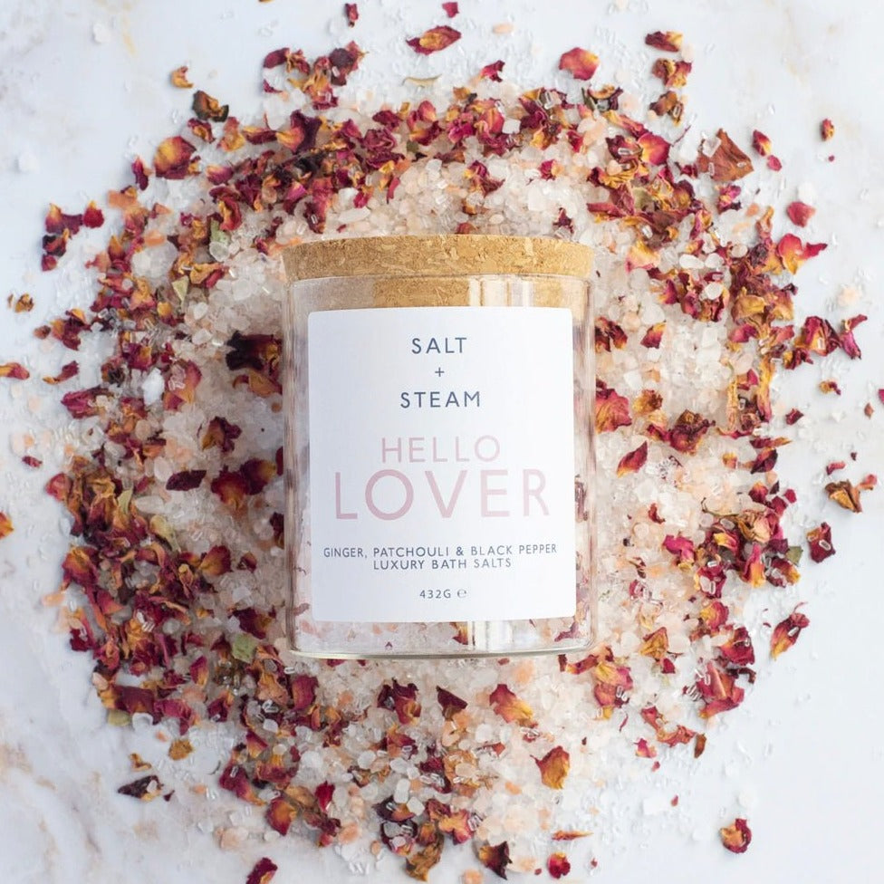 Glass jar of bath salts with a cork lid, laid on a pile of salt crystals and rose petals