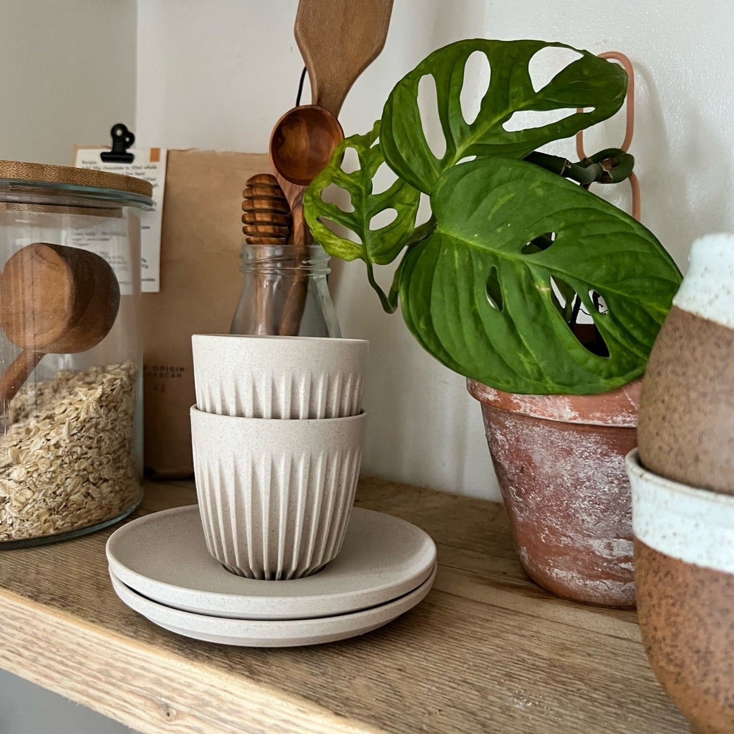2 handleless espresso cups stacked together on a kitchen shelf, beside a jar of oats
