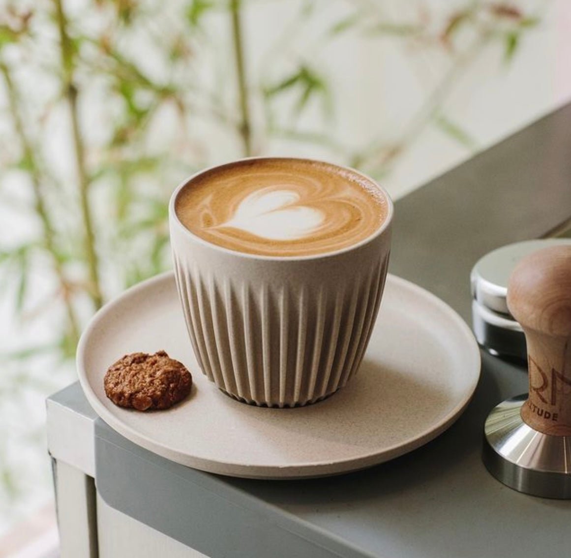 a cream cup with lined sides, holding a latte, sat on a cream saucer