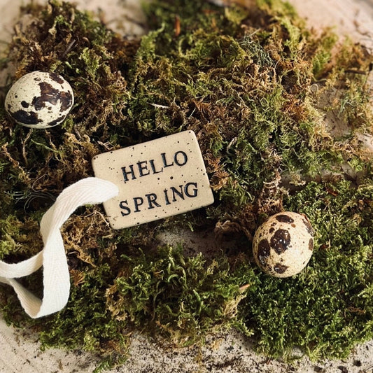 ceramic tag on a bed of moss with yellow candles burning in the background