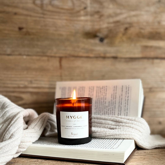 amber jar candle lit on an open book beside a cosy jumper