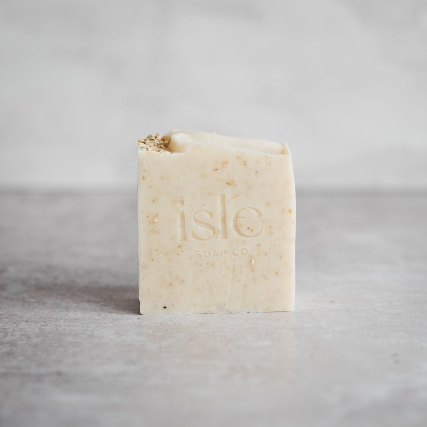 A square shaped block of soap, cream in colouring with a scattering of oats on top